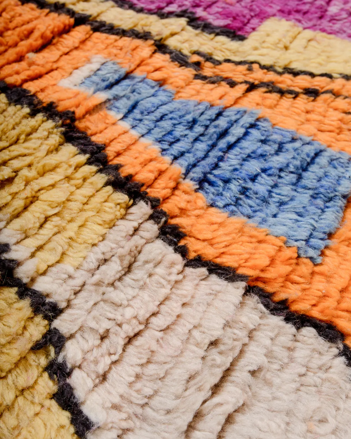 Detail of woolen rug texture in orange, blue, cream, yellow, black and pink.